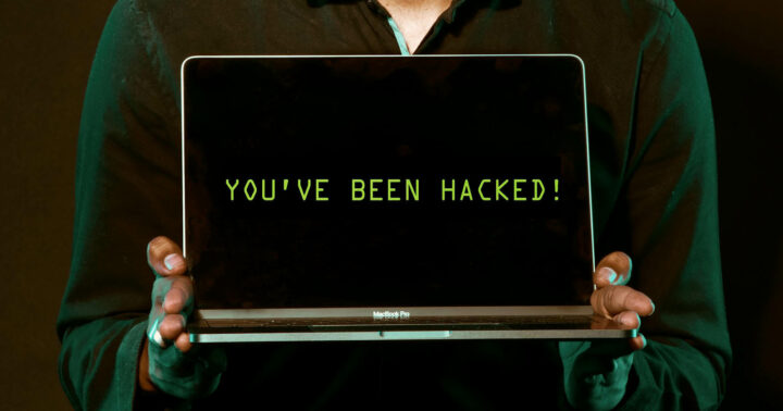 På bilden syns en person som står och håller i en dator. På datorn står det You have been hacked.