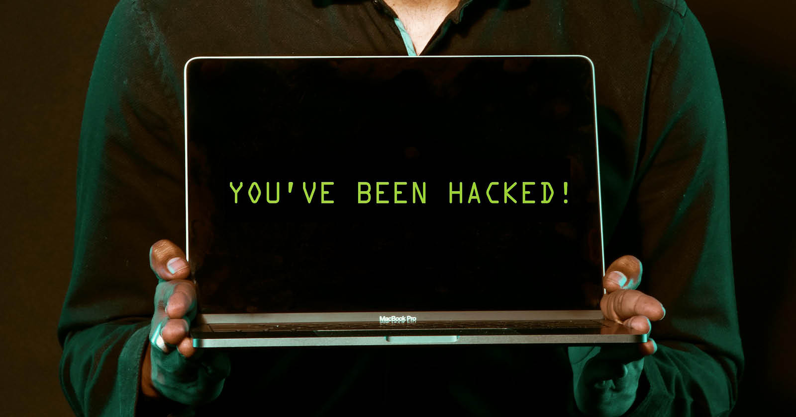 På bilden syns en person som står och håller i en dator. På datorn står det You have been hacked.