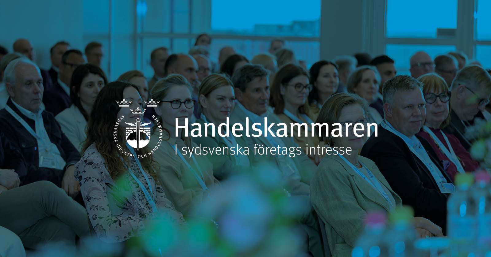 Bild över en publik. Bilden har ett blått lager med Handelskammarens logga i mitten